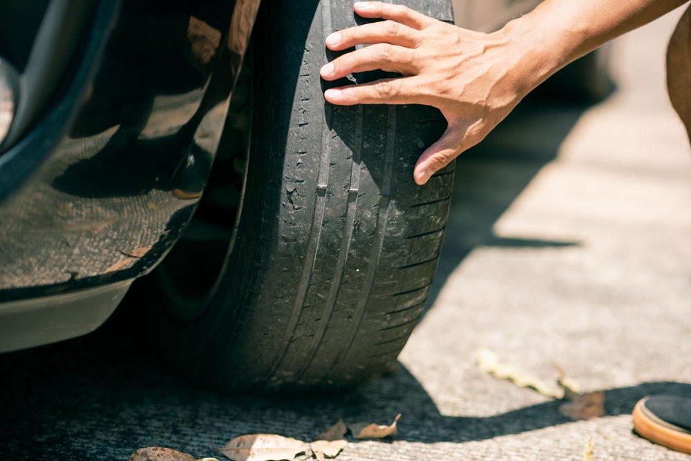 Image of a person‘s hand examining the tyre tread depth of the front left tyre on a car.
