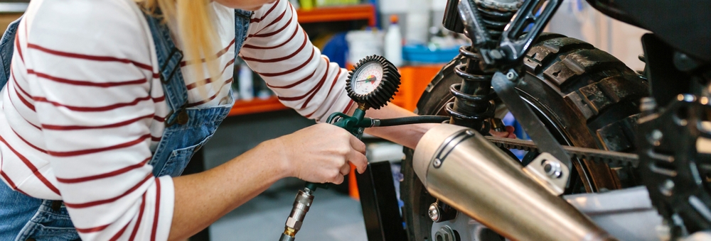 A mechanic checking the tyre air pressure of a motorcycle.
