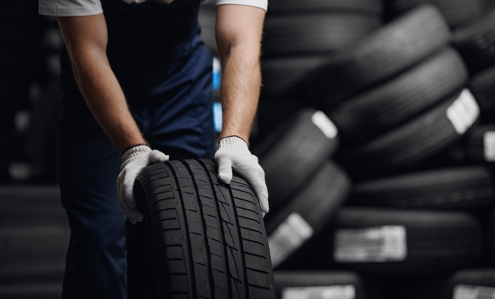 Close-up of a mechanic with white gloves holding onto a black car tyre.